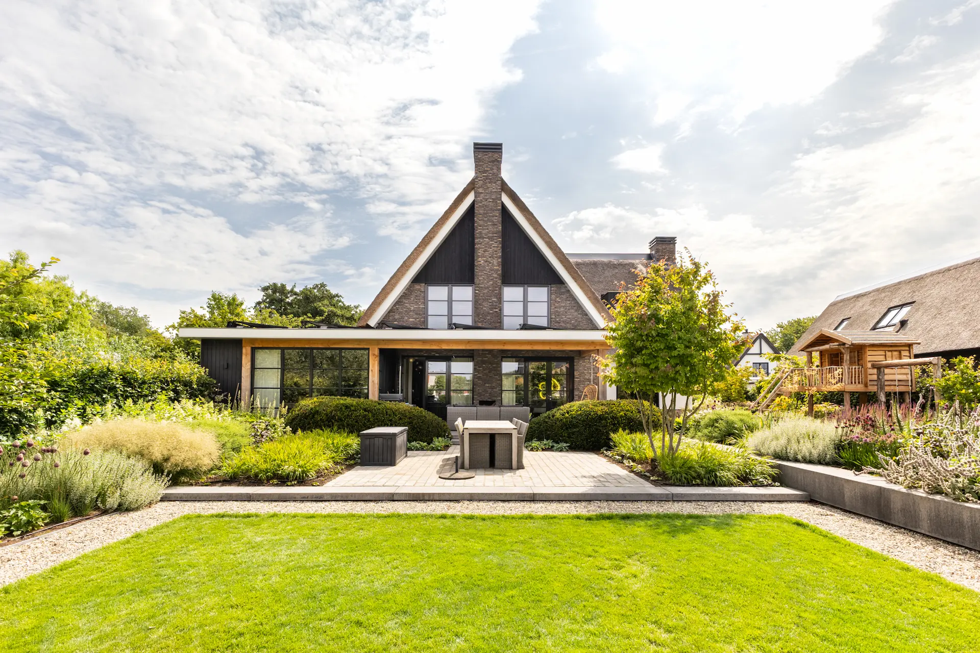 Achterzijde van rietgedekte moderne villa met brede veranda, grote glaspuien en strakke tuin, ontworpen door ervaren architect Oud-Alblas.