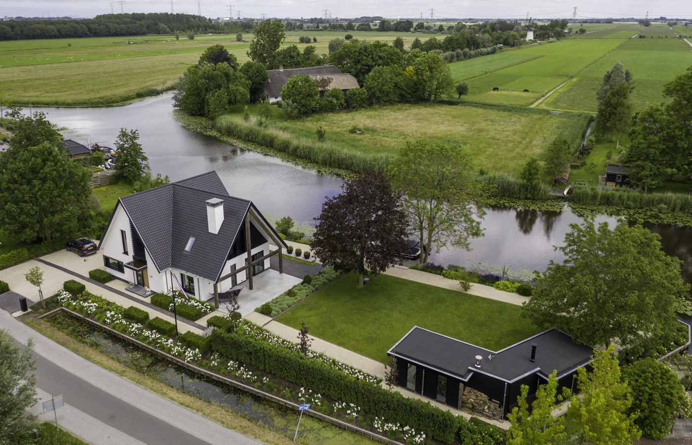 Luchtfoto van woningrenovatie aan het water met wit stucwerk en zwarte kap &ndash; ontwerp door architect Bongers in landelijke omgeving.