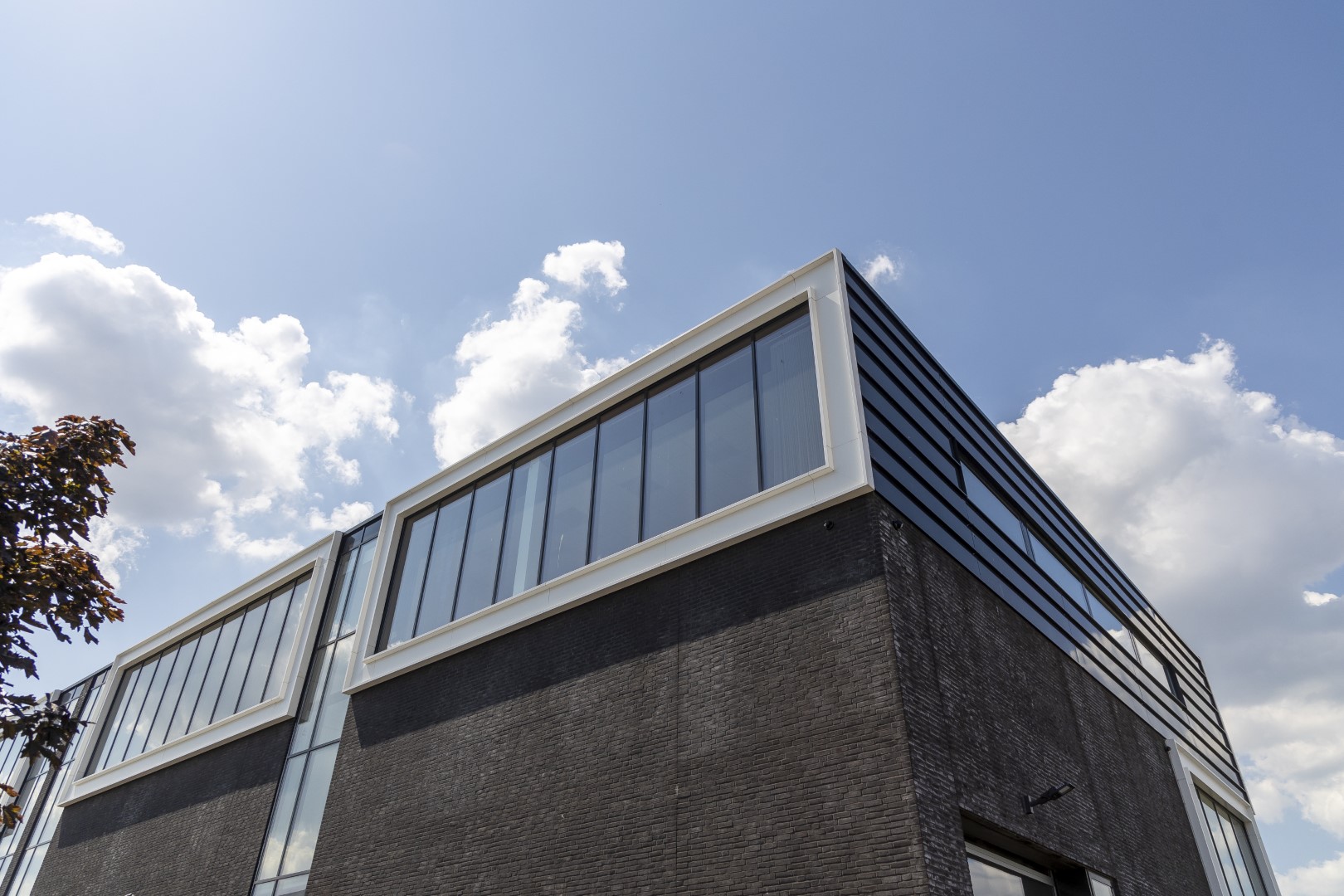 Bedrijfsunit met moderne hoekoplossing, donkere gevelsteen en doorlopende glasstroken &ndash; architect voor bedrijfspand ontwerpen