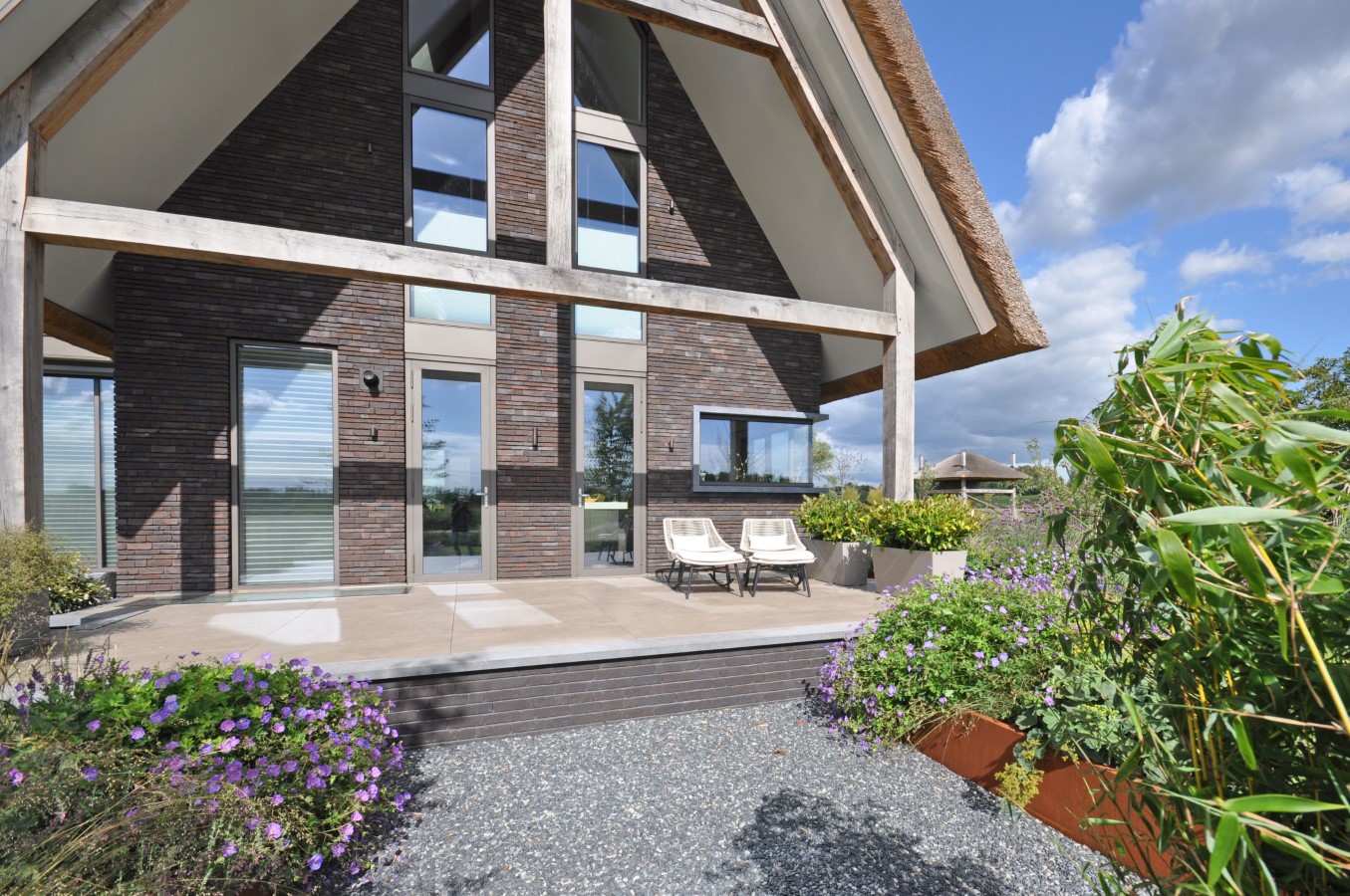Rietgedekte villa met grote glaspartijen en houten spanten &ndash; duurzaam huis ontwerpen met licht en zicht in architectuur.