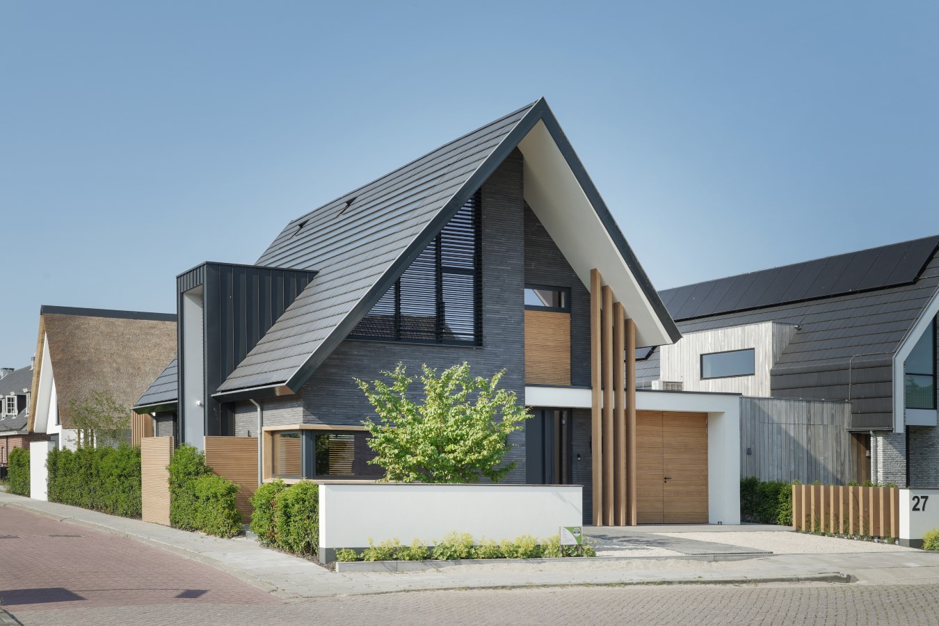 Moderne woning met asymmetrisch zadeldak, donkere gevelstenen en verticale houten details &ndash; strak ontwerp in woonwijk.