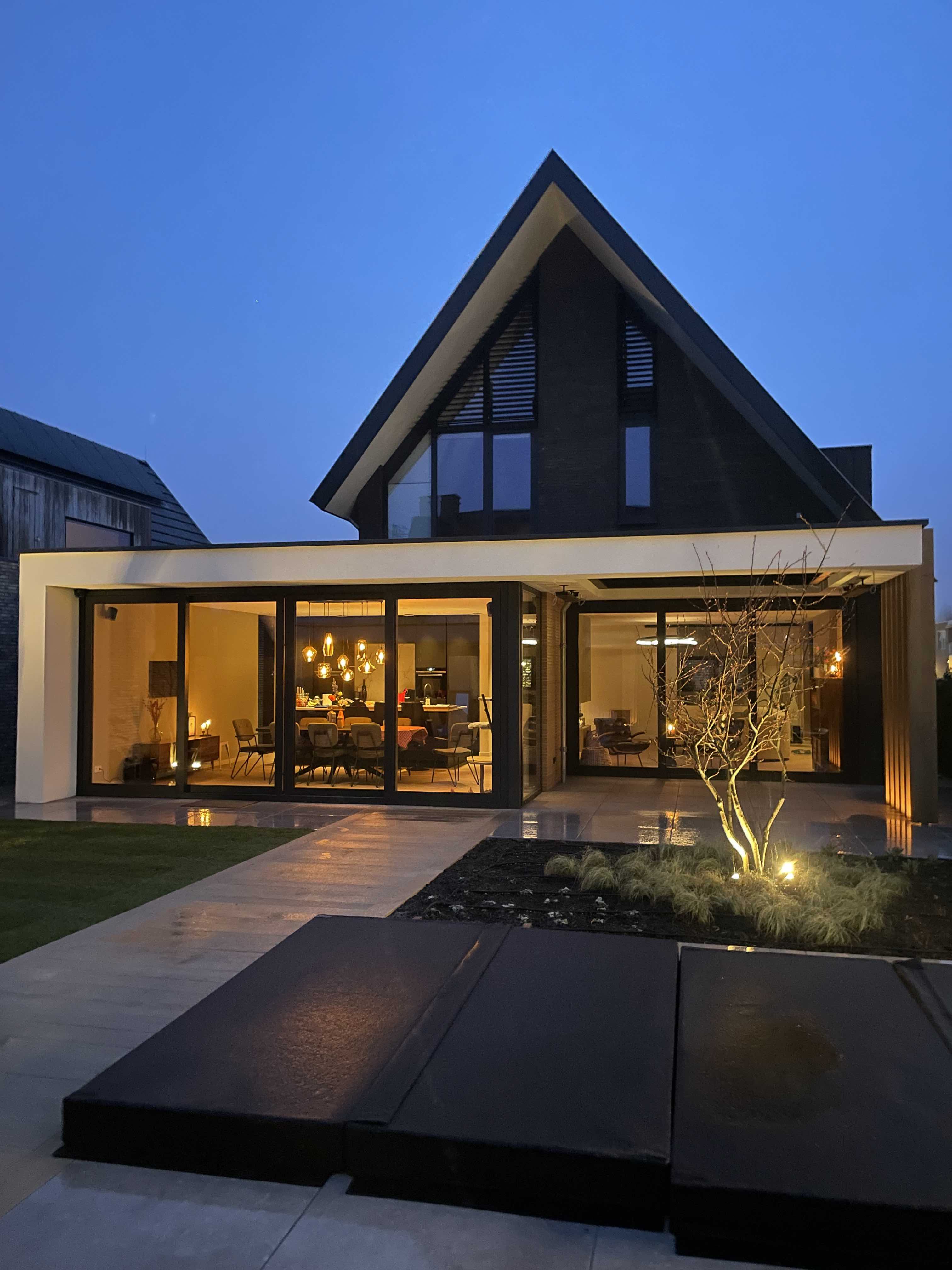 Verlichte moderne villa in de avond met grote glaspuien en strakke aanbouw &ndash; duurzaam huis ontwerpen met zichtlijnen en maatwerk door architect Oud-Alblas.