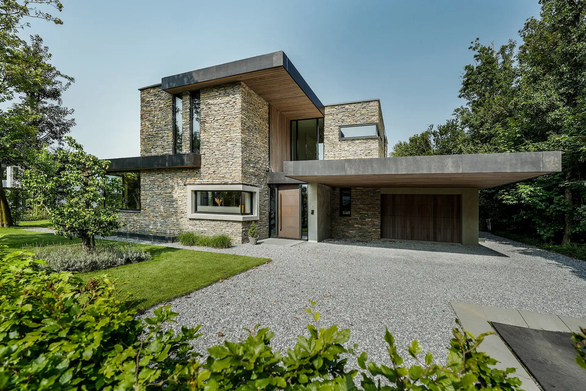 Moderne villa met natuurstenen gevels, grote overstekken en houten accenten &ndash; duurzaam en sculpturaal ontwerp door Bongers Architecten