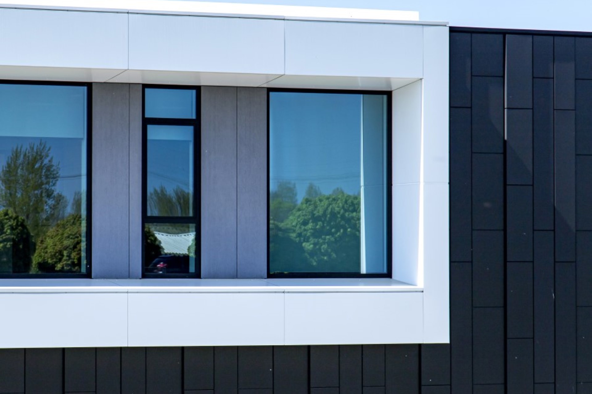 Detail moderne gevel met witte kaders, grote ramen en zwarte beplating &ndash; strak en modern bedrijfspand ontwerpen.