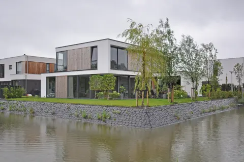 Strakke witte watervilla met houten gevelbekleding, grote raampartijen en groene tuin &ndash; duurzaam en eigentijds ontwerp door Bongers Architecten