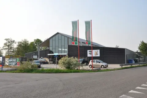Bedrijfsruimte met asymmetrisch zadeldak, houten gevelbekleding en hoge glaspartij &ndash; maatwerk bedrijfsarchitectuur.