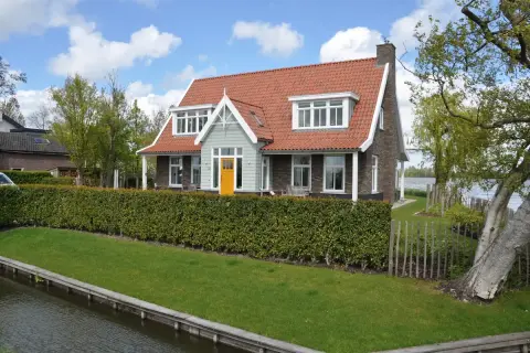Landelijke villa aan het water met rode dakpannen, wit houtwerk en een opvallende gele voordeur &ndash; klassieke stijl met moderne accenten