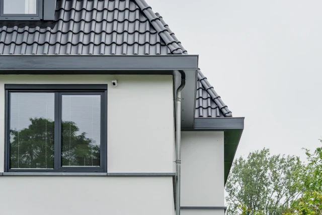 Geveldetail met wit stucwerk, donker kozijn en keramische dakpannen &ndash; woningontwerp door architect Alblasserwaard.
