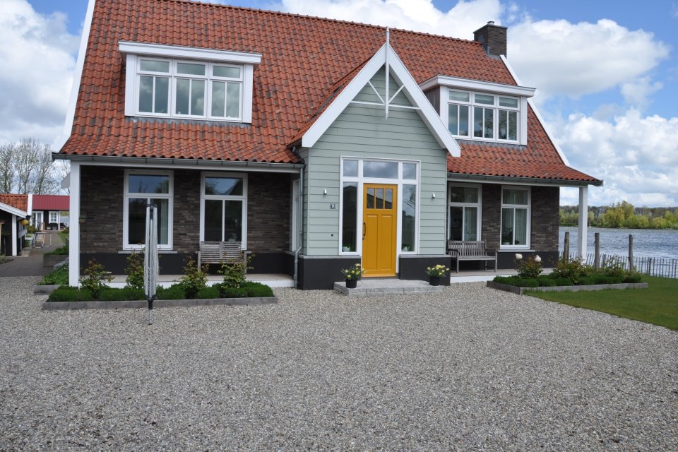 Woning aan het water met rood pannendak, gele voordeur en grote dakkapellen &ndash; architect Oud-Alblas met oog voor licht en zicht in architectuur.