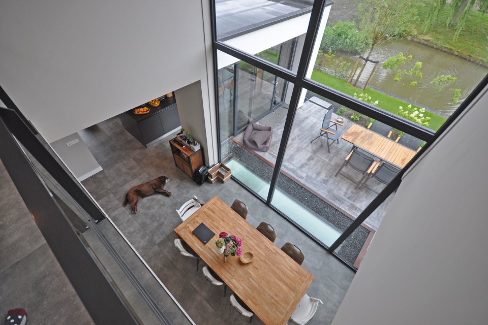 Moderne woning met vide en hoge glaspuien die zicht bieden op terras en water &ndash; ontwerp door architect Bongers Architecten