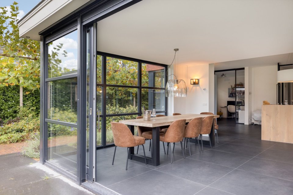 Uitbouw met glazen schuifpuien en eethoek &ndash; licht en zicht in architectuur cre&euml;ren een naadloze overgang tussen binnen en buiten