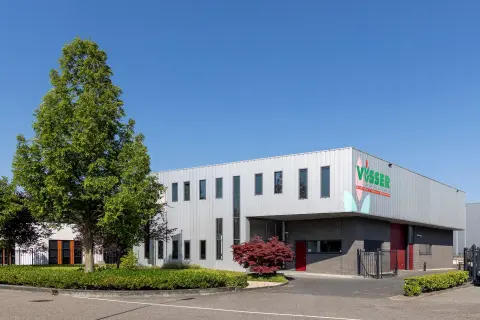 Modern bedrijfsgebouw van Visser met strakke metalen gevelbekleding, rode accenten en een groene omgeving