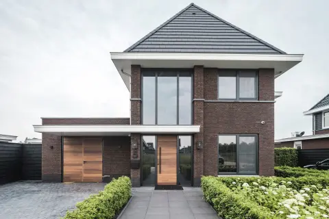 Strakke villa met donkere baksteen, houten accenten en hoge raampartijen &ndash; eigentijds ontwerp door architect in Nederland