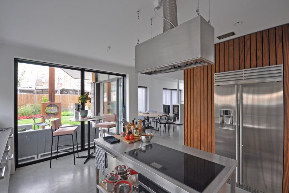 Moderne keuken met rvs-details, houten lattenwand en zicht op tuin &ndash; woning ontworpen door ervaren architectenbureau Bongers Architecten