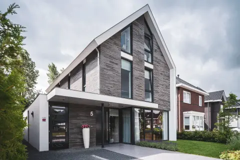 Strakke moderne woning met asymmetrisch zadeldak, verticale gevelbekleding en veel glas &ndash; eigentijdse architectuur in Zuid-Holland