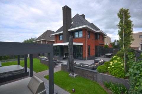 Achtertuin van moderne villa met rood metselwerk, strakke lijnen, grote glaspartijen en groene tuin &ndash; ontwerp Bongers Architecten