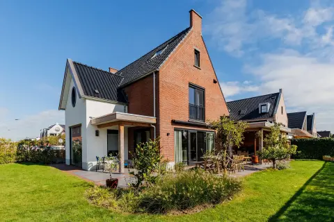 Klassieke vrijstaande woning met rode bakstenen gevel, zwarte kap en zonnige tuin in een groene woonwijk.