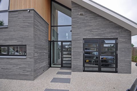 Strakke entree met verticale baksteen, houten gevelaccent en glaspartij &ndash; ontworpen door ervaren architectenbureau Bongers Architecten