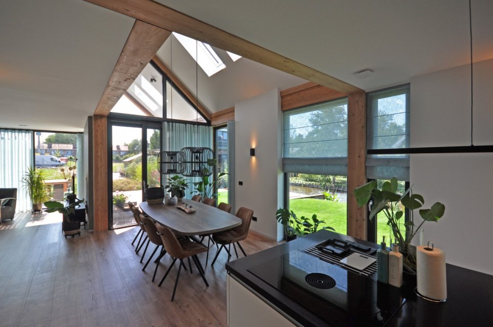 Lichte eetruimte met vide, houten spanten en zicht op tuin en water &ndash; duurzaam huis ontwerpen met licht en zicht in architectuur